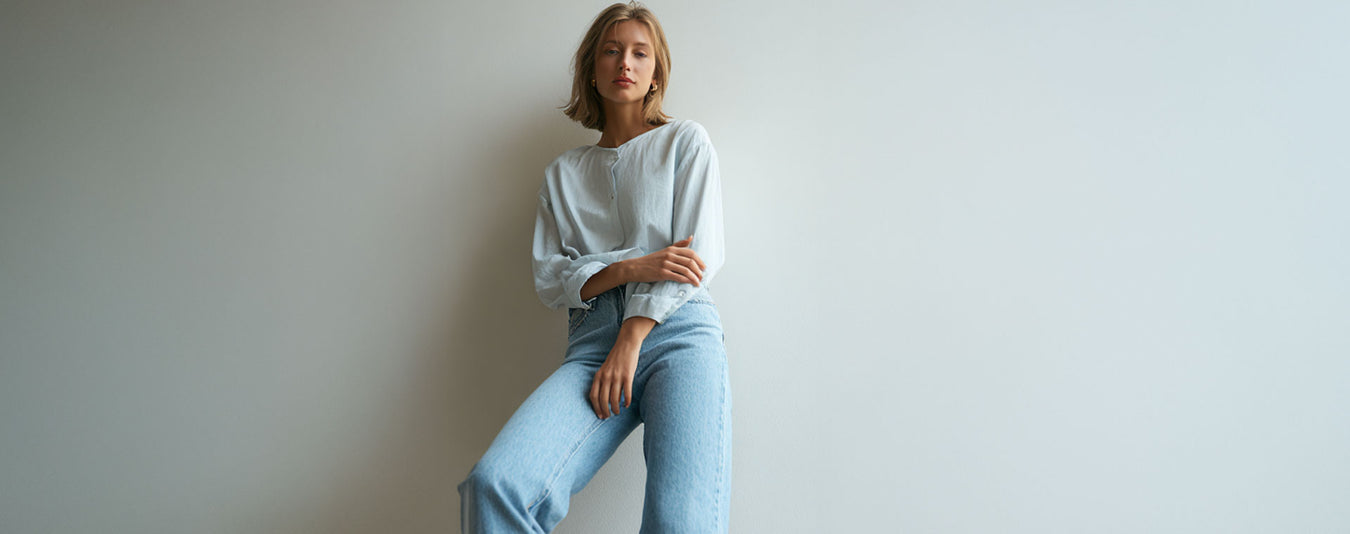 Woman wearing a white sweater and light blue jeans against a plain background